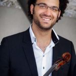 Person wearing a white button up shirt and dark jacket, holding a viola