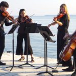 4 young students playing string instruments on a dock