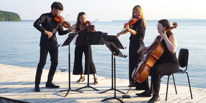 4 young students playing string instruments on a dock