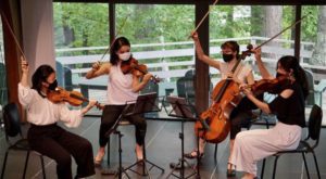 Four string players on a stage, holding their bows in the air