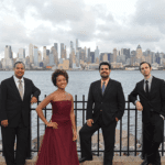 4 people standing together with New York skyline behind them.