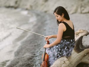 Person sitting on a beach holding a violin